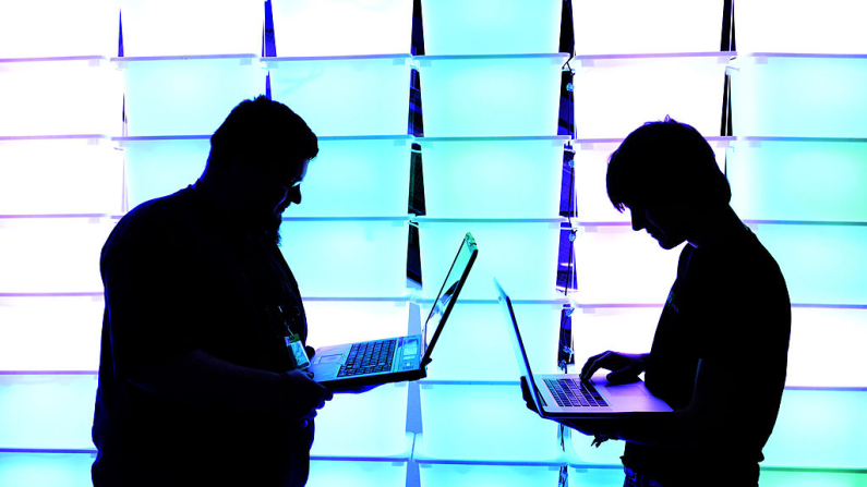 Participantes sostienen sus portátiles frente a una pared iluminada. Imagen de archivo. (Patrick Lux/Getty Images)