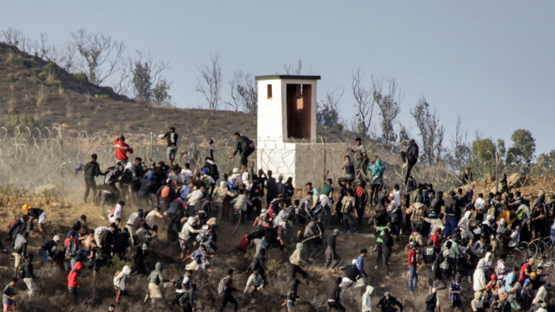Migrantes asaltan una valla de alambre de púas al intentar cruzar la frontera terrestre con el enclave africano español de Ceuta, cerca de Fnideq, en el norte de Marruecos, el 15 de septiembre de 2024. (Foto de AFP vía Getty Images)