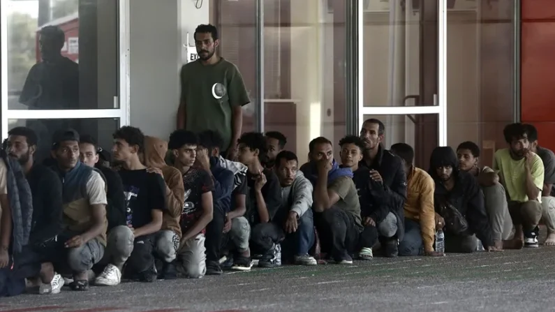 Refugiados e inmigrantes se sientan frente a la autoridad portuaria griega tras ser transportados desde un granelero en el puerto de Lavrio, Grecia. EFE/EPA/Yannis Kolesidis