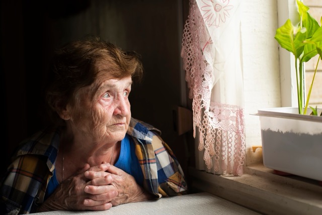 Una anciana solitaria mira fijamente por la ventana. Foto de Shutterstock, Inc.