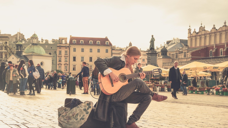 Un joven toca la guitarra en medio de una plaza rodeada de personas. Pexels. Pixabay