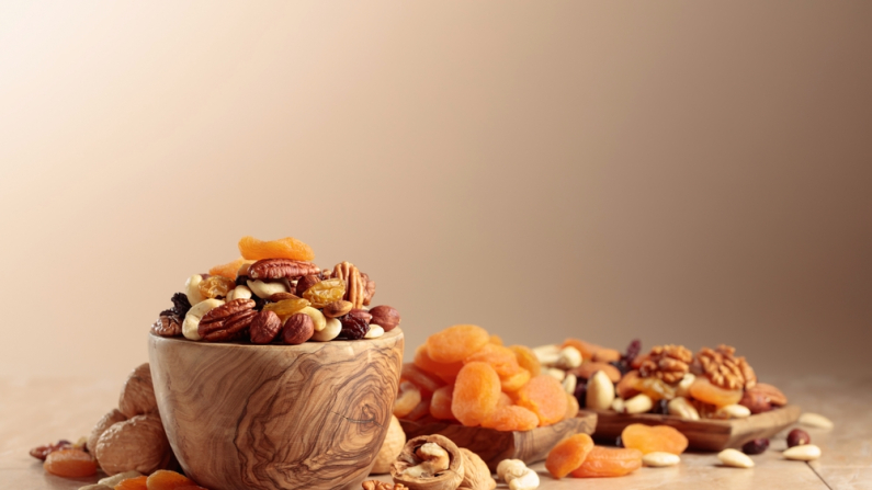 Frutas y frutos secos sobre una mesa de cerámica beige. La mezcla de nueces, albaricoques y pasas en un tazón de madera. Copiar espacio.