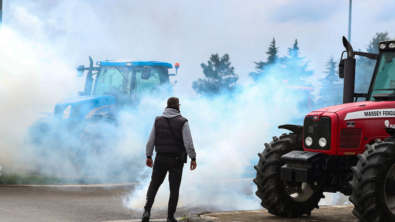 TOPSHOT - Un manifestante se encuentra en medio del humo del gas lacrimógeno lanzado por la policía antidisturbios mientras los agricultores bloquean la carretera que conduce al aeropuerto con sus tractores durante una protesta por la reducción y el retraso en el pago de las subvenciones de la Unión Europea, en Tesalónica, el 5 de diciembre de 2025. (Foto de AFP vía Getty Images)